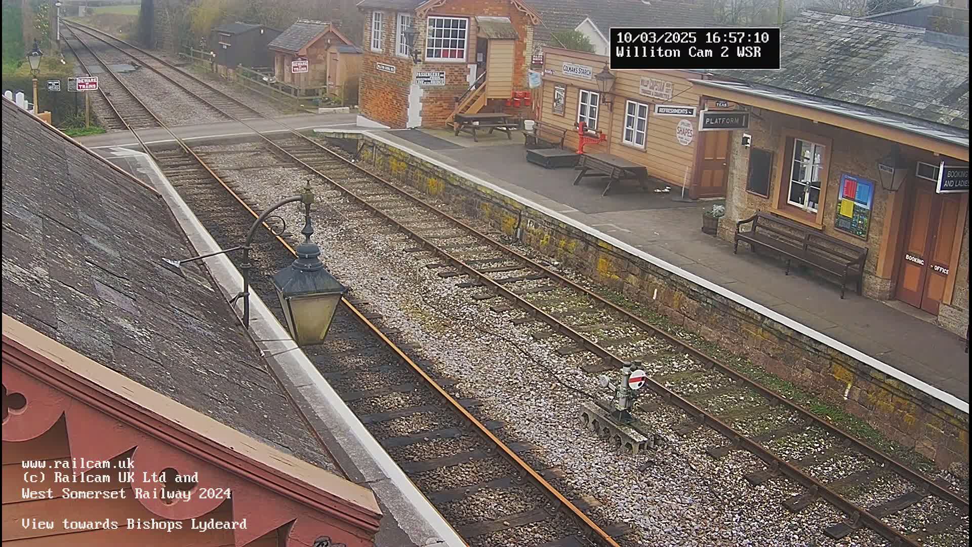 A train station platform with multiple tracks, a small building, and a bench under an overcast sky.