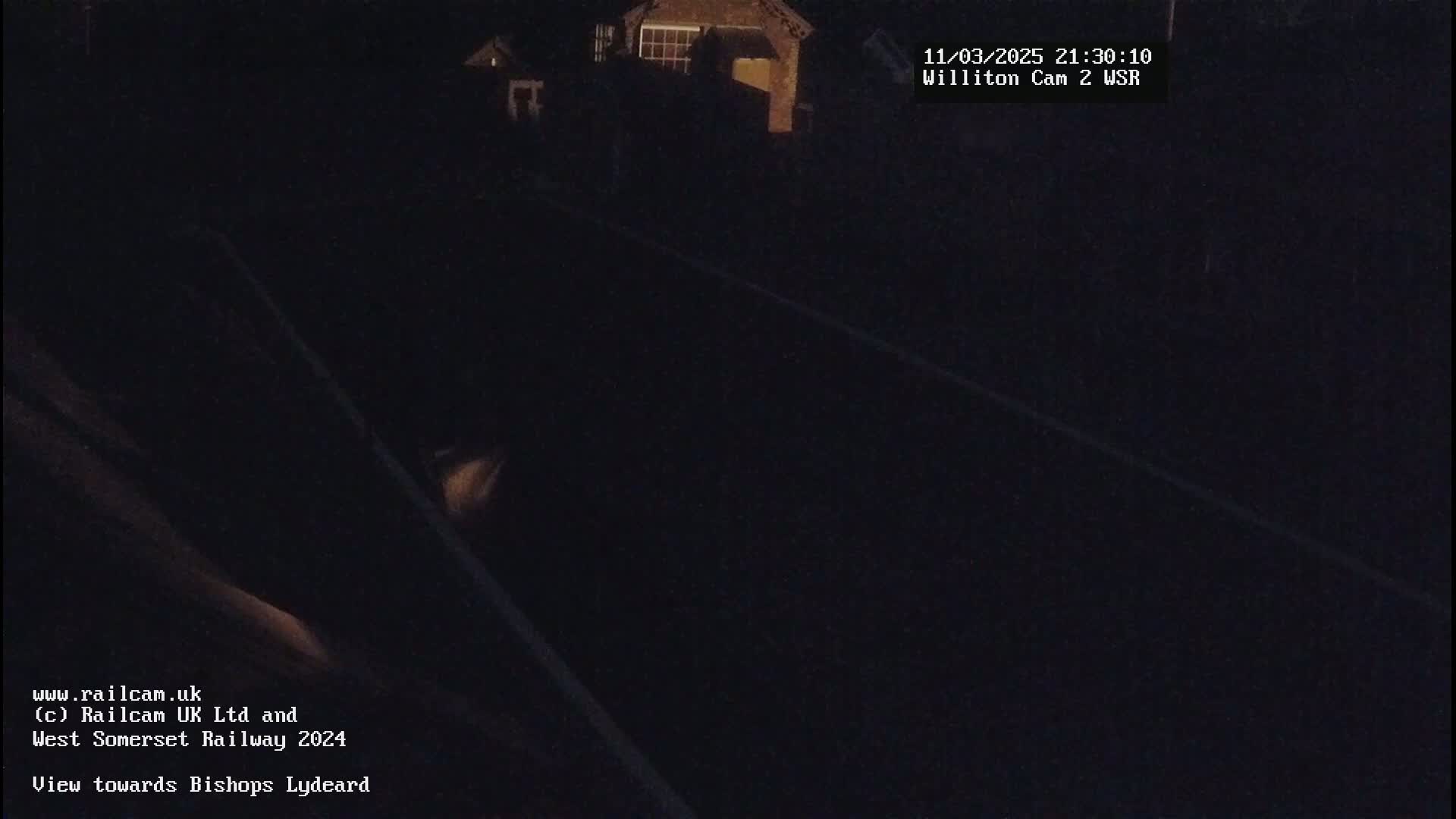 A dark, nighttime view of train tracks and a building in the distance.