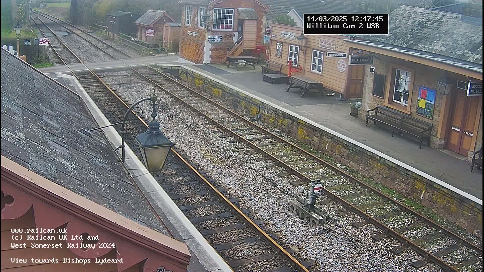 A train station with two train tracks and a platform, on an overcast day, is viewed from a slightly elevated angle.