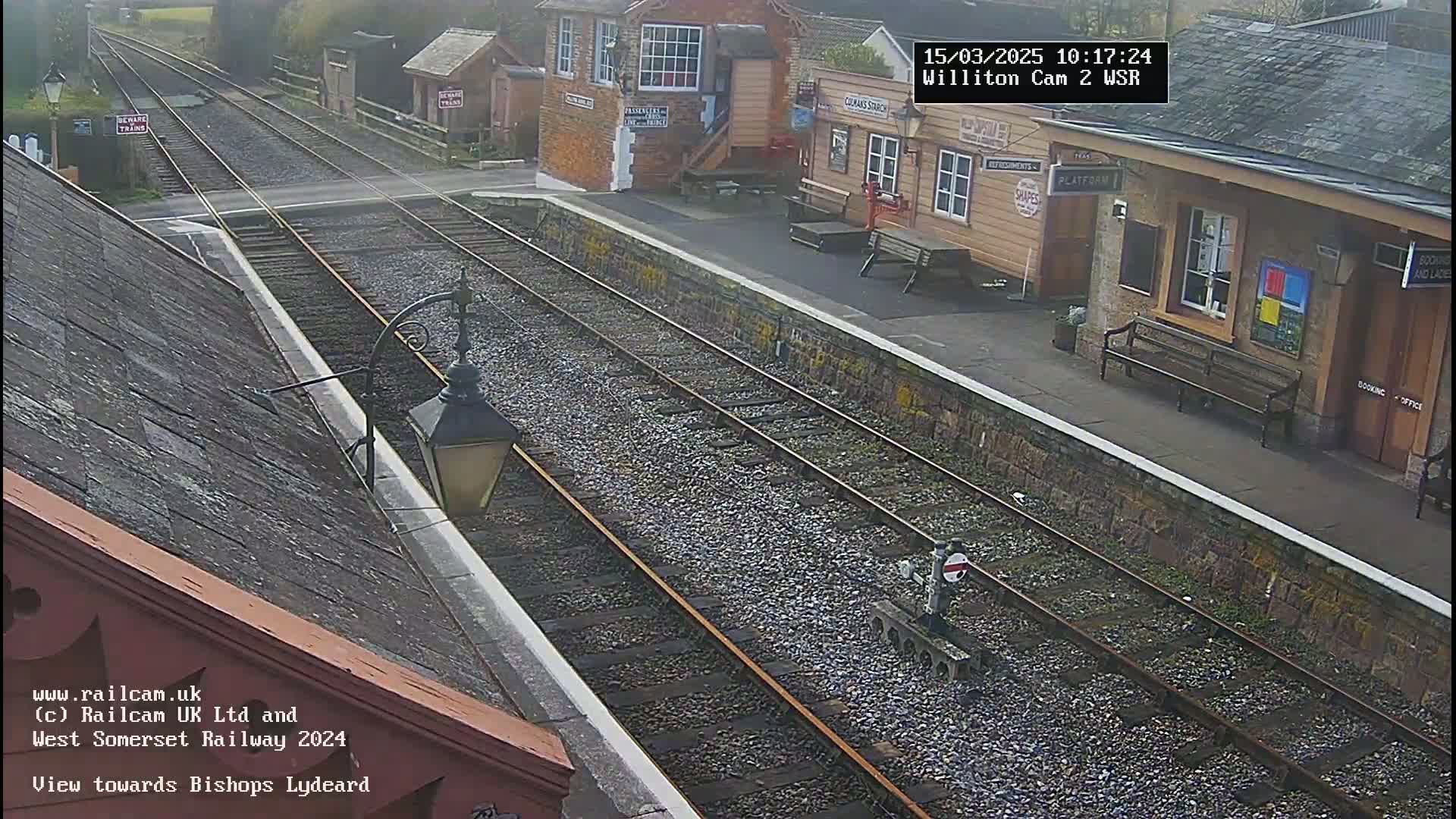 A high-angle view of a train station platform with two parallel train tracks extending into the distance on an overcast day.