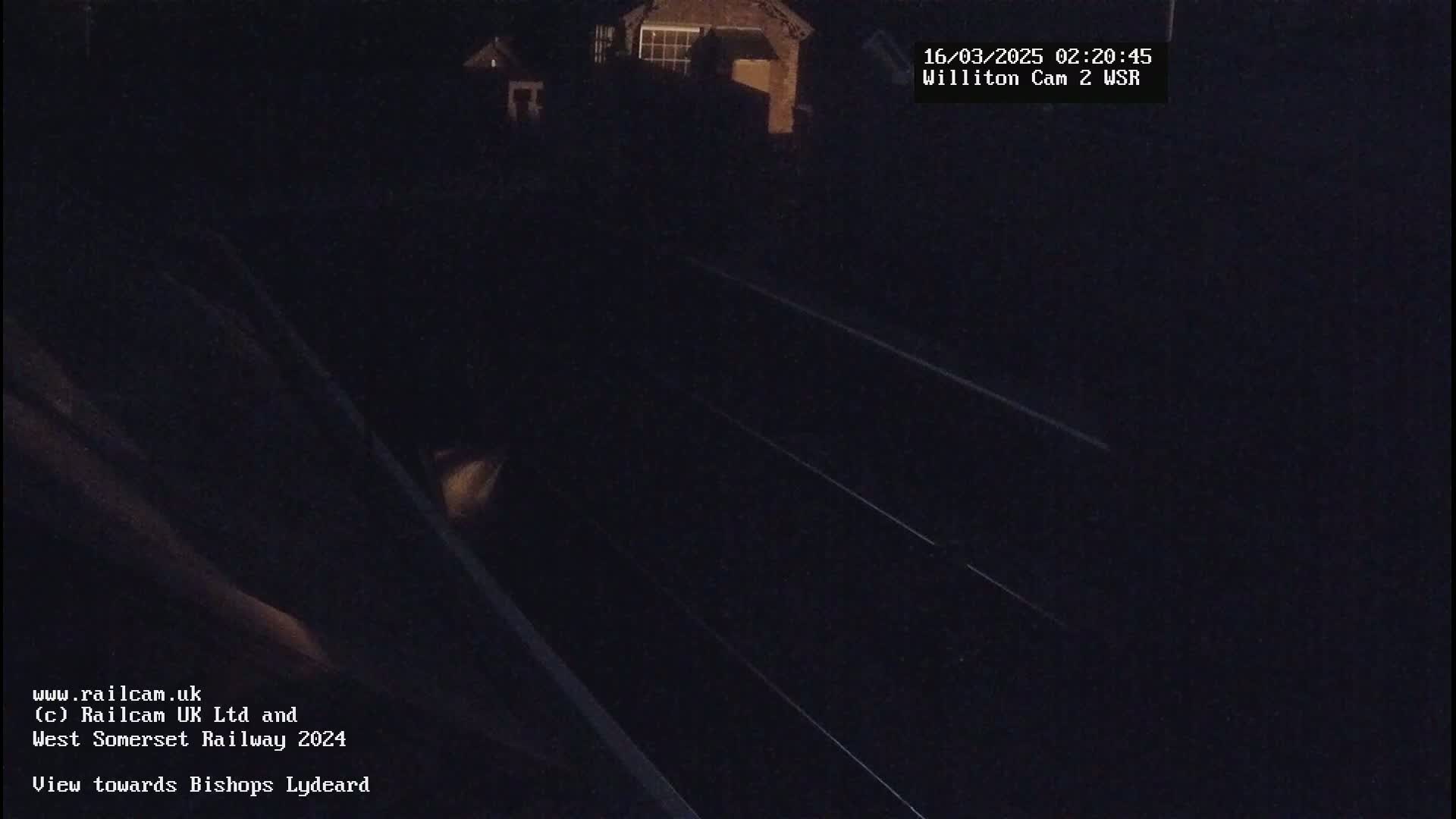 A nighttime, low-light view of train tracks and a building in the distance.