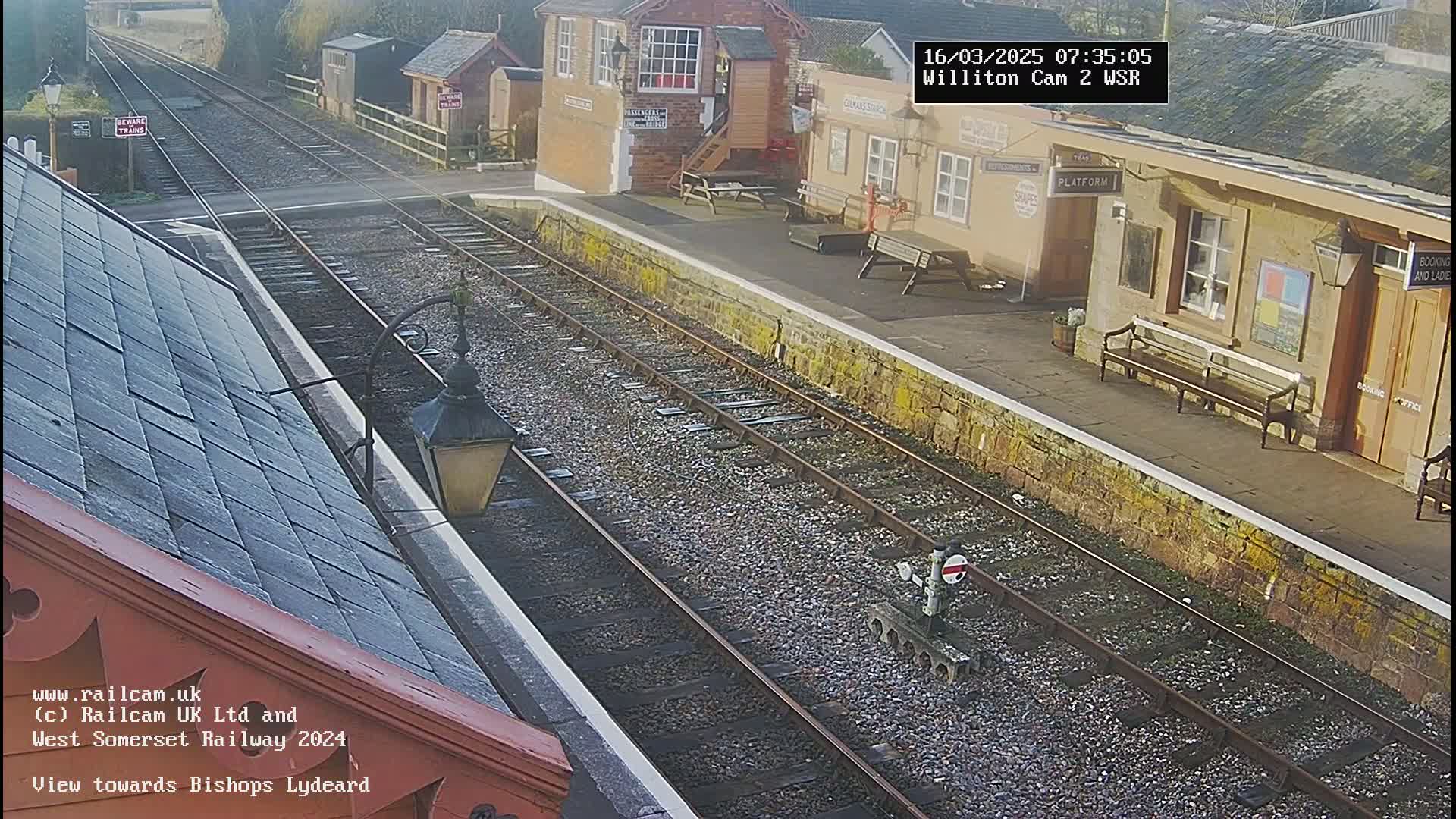 A sunny view of a train station platform with railway tracks extending into the distance.