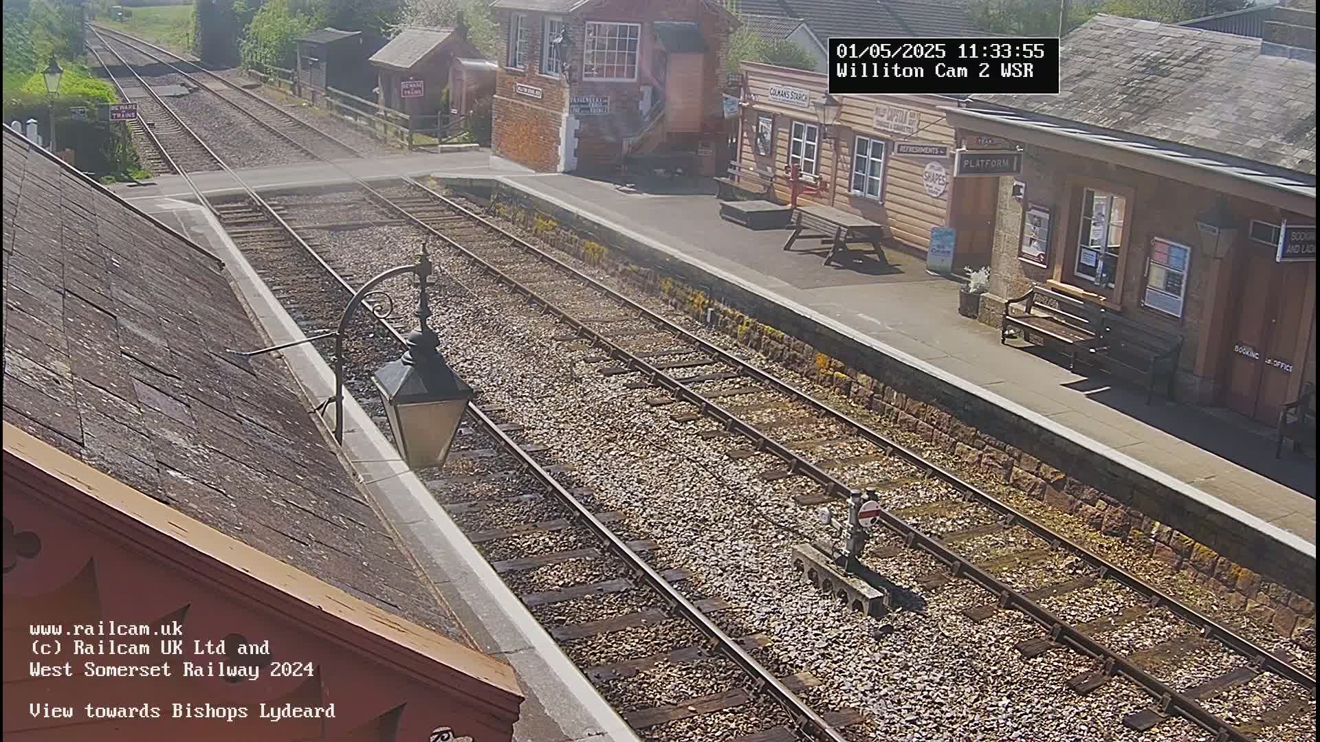 A sunny view of a train station platform with railway tracks extending into the distance.