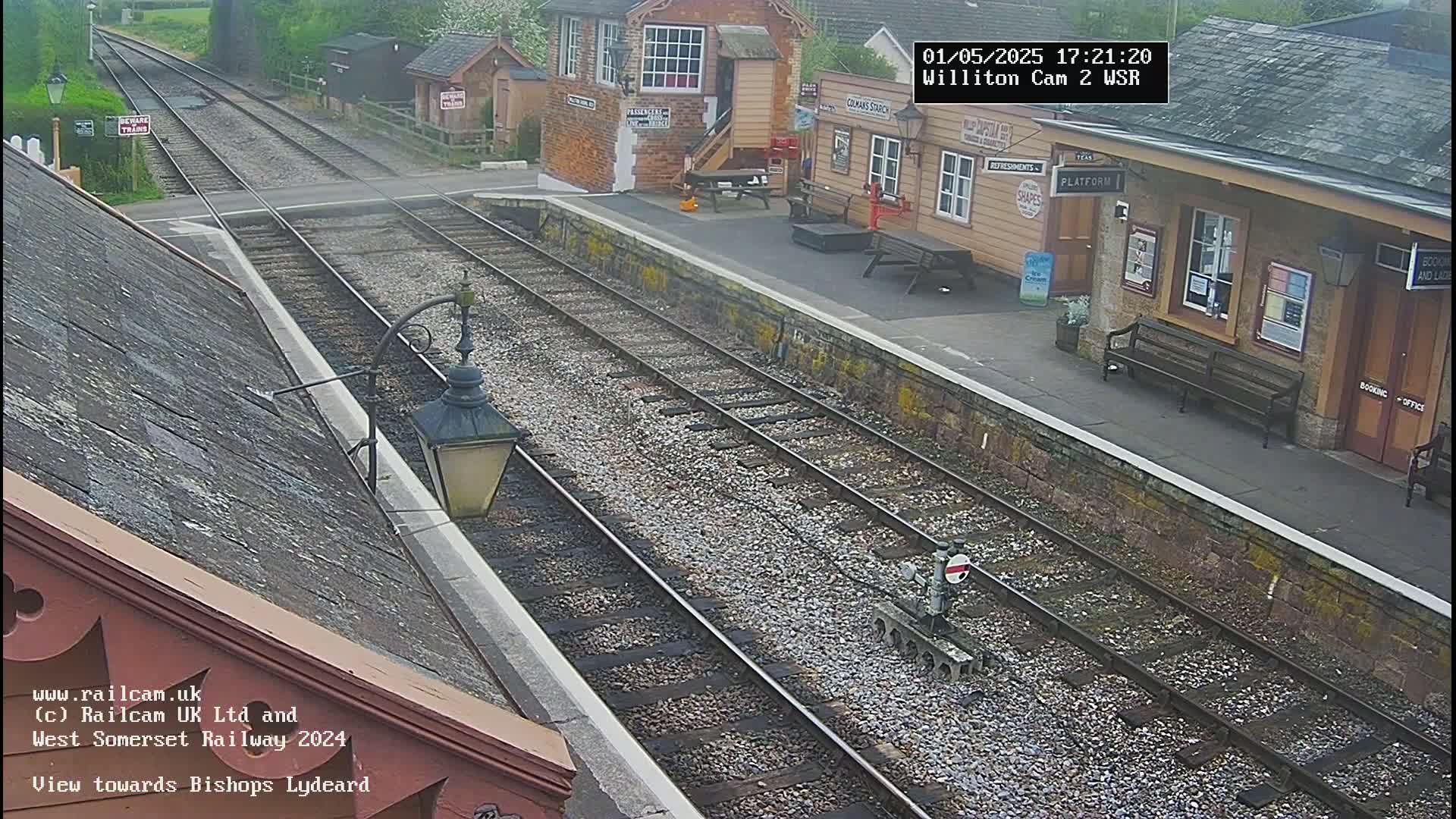 A train station platform with two parallel train tracks, viewed from an elevated angle, on an overcast day.