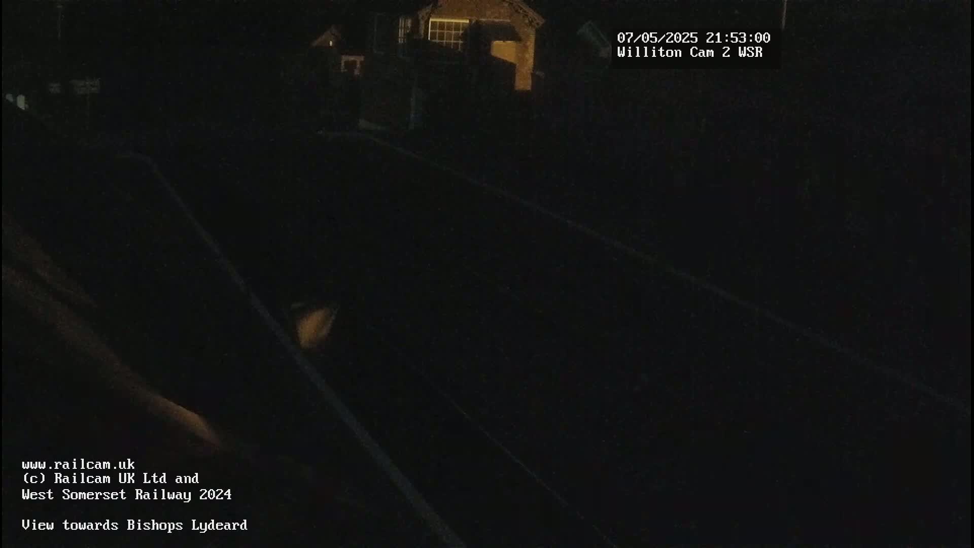 A dark, nighttime view of a railway line, with dimly lit buildings in the background.