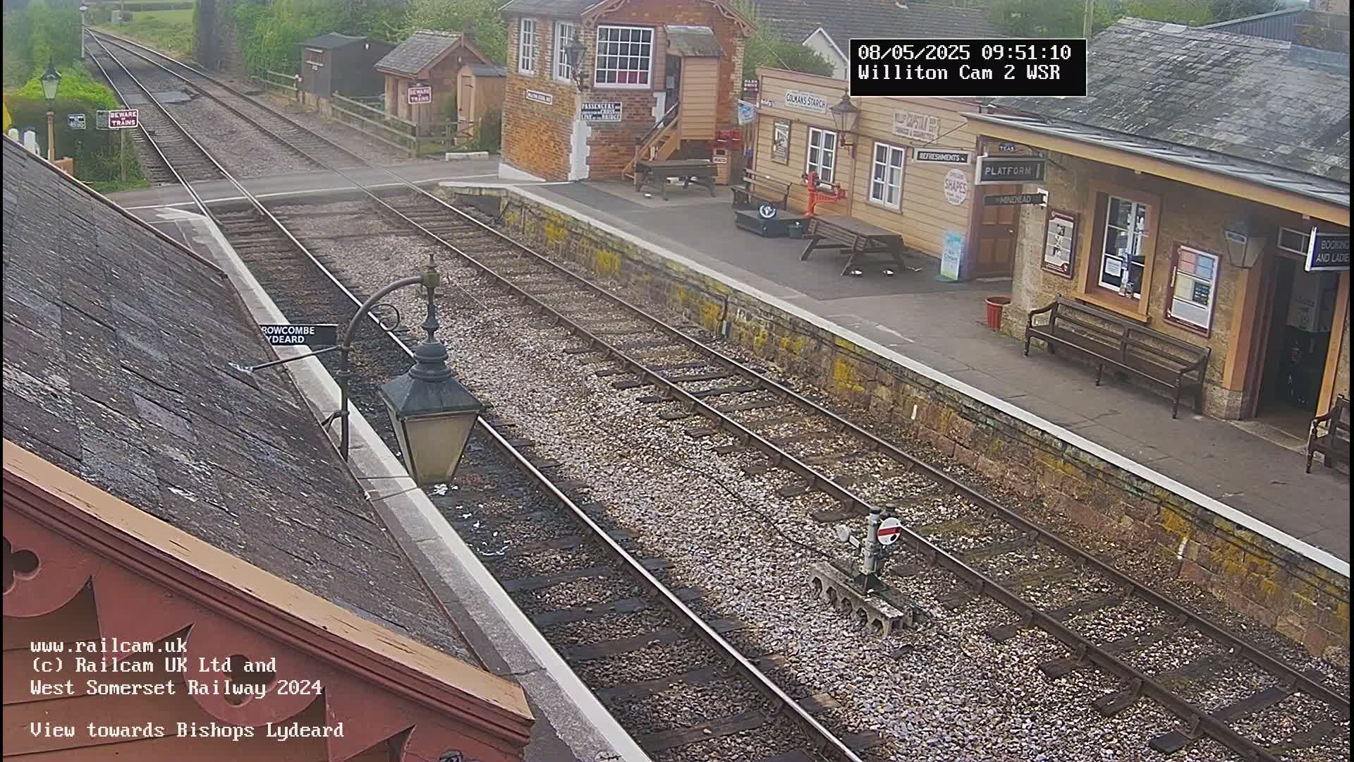 A view of a train station platform and railway tracks on an overcast day.