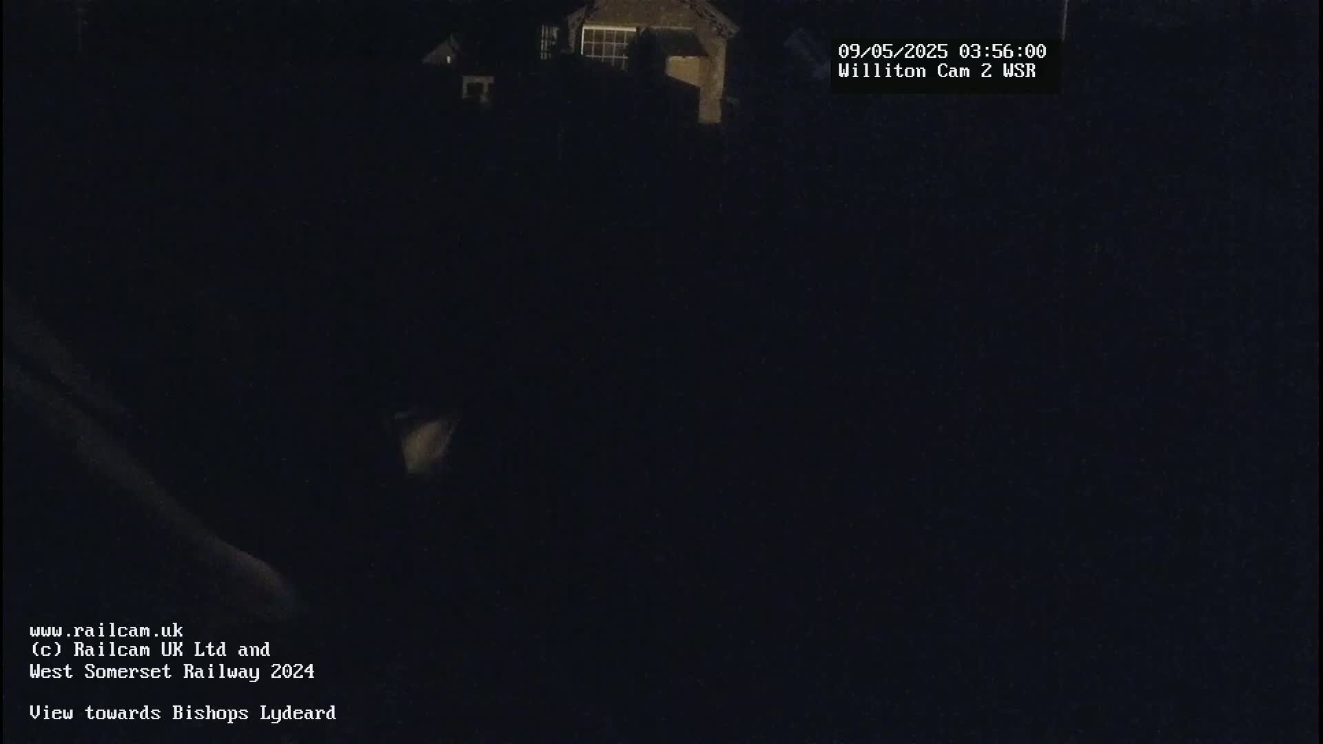 A dark, nighttime scene shows a dimly lit building in the distance.