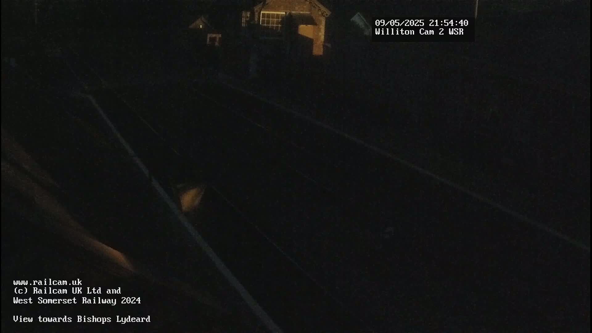 A nighttime, low-light view of dark train tracks and a dimly lit building in the distance.