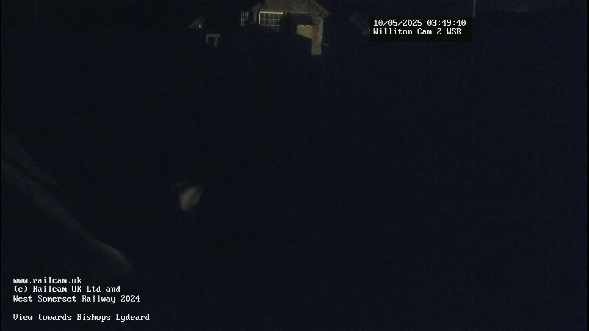 A nighttime, dark image shows a small portion of a building in the upper right corner, with the rest of the view obscured by darkness.