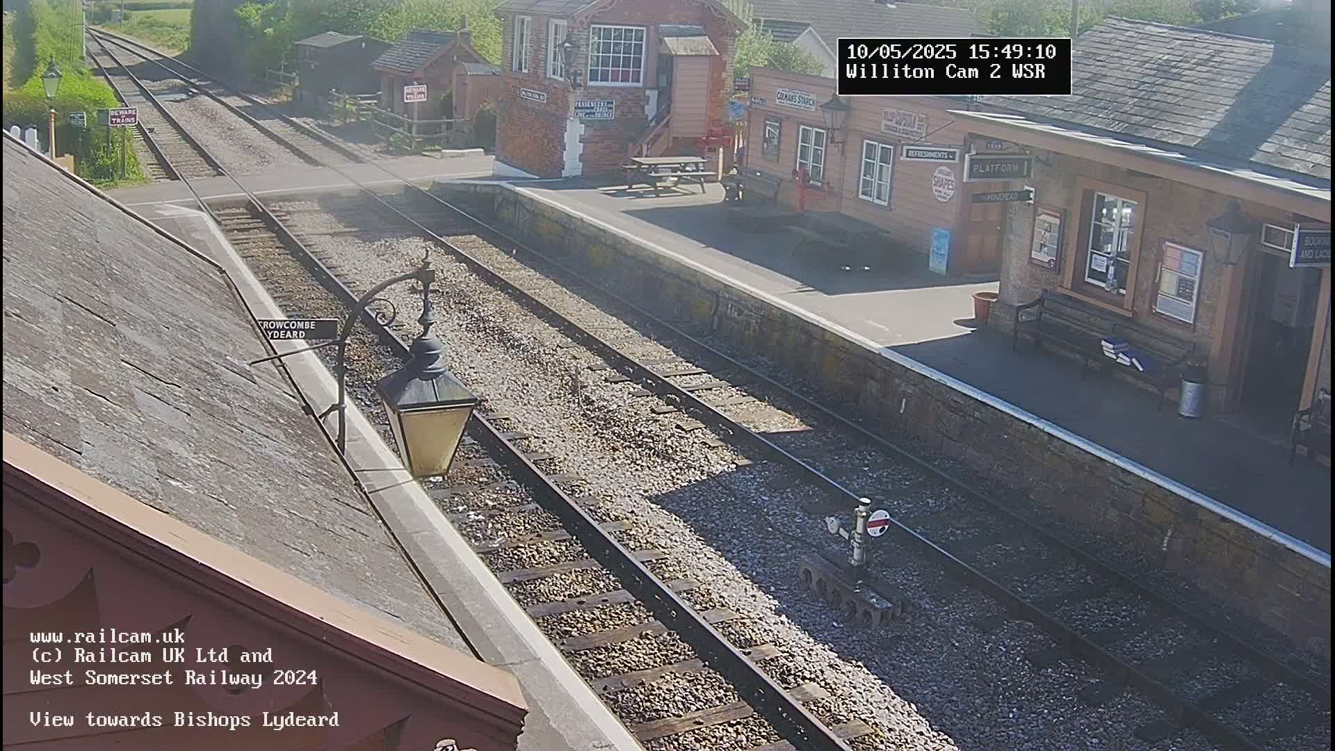 A sunny view of a train station platform with two sets of train tracks extending into the distance.