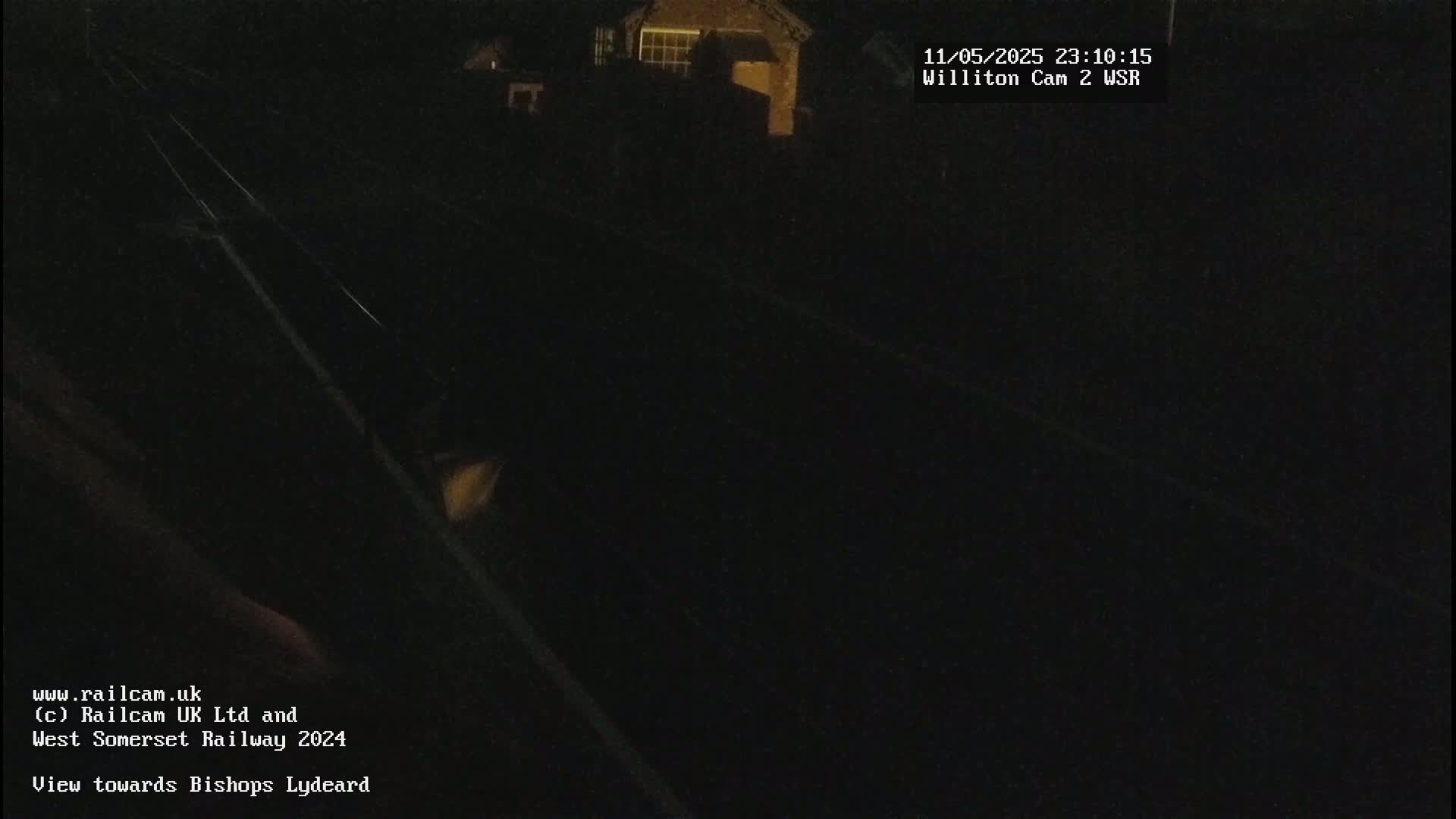 A dark nighttime view of railroad tracks and a dimly lit building in the distance.
