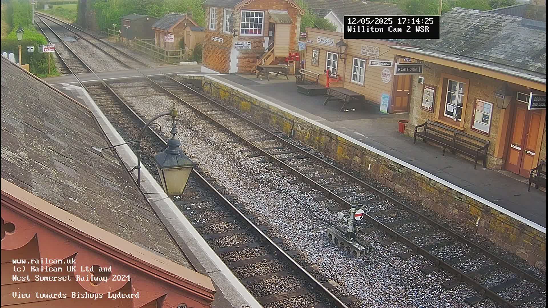 A railway station platform with two sets of tracks, a station building, and overcast outdoor conditions.