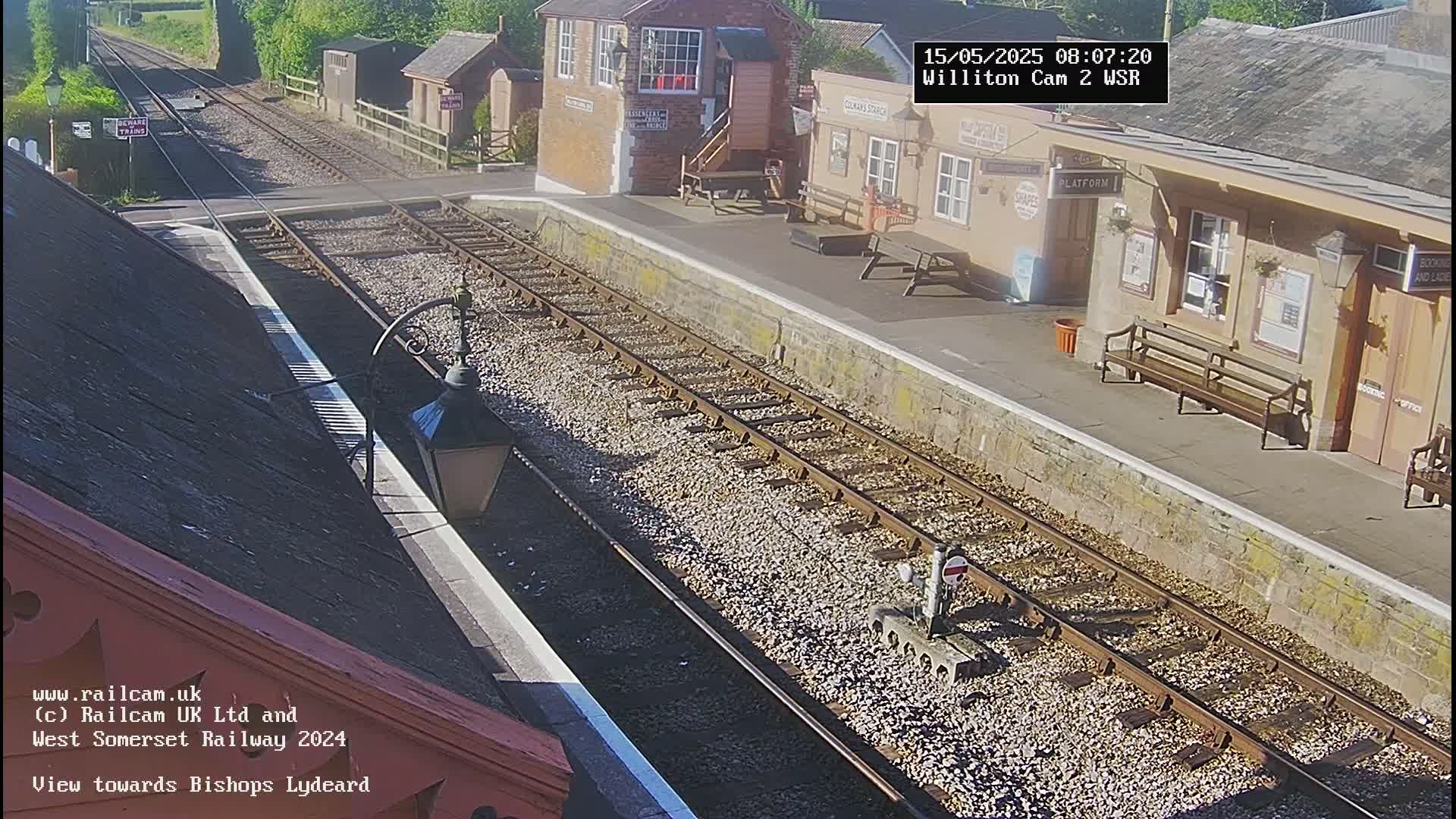 A sunny view of a train station platform with railway tracks extending into the distance.