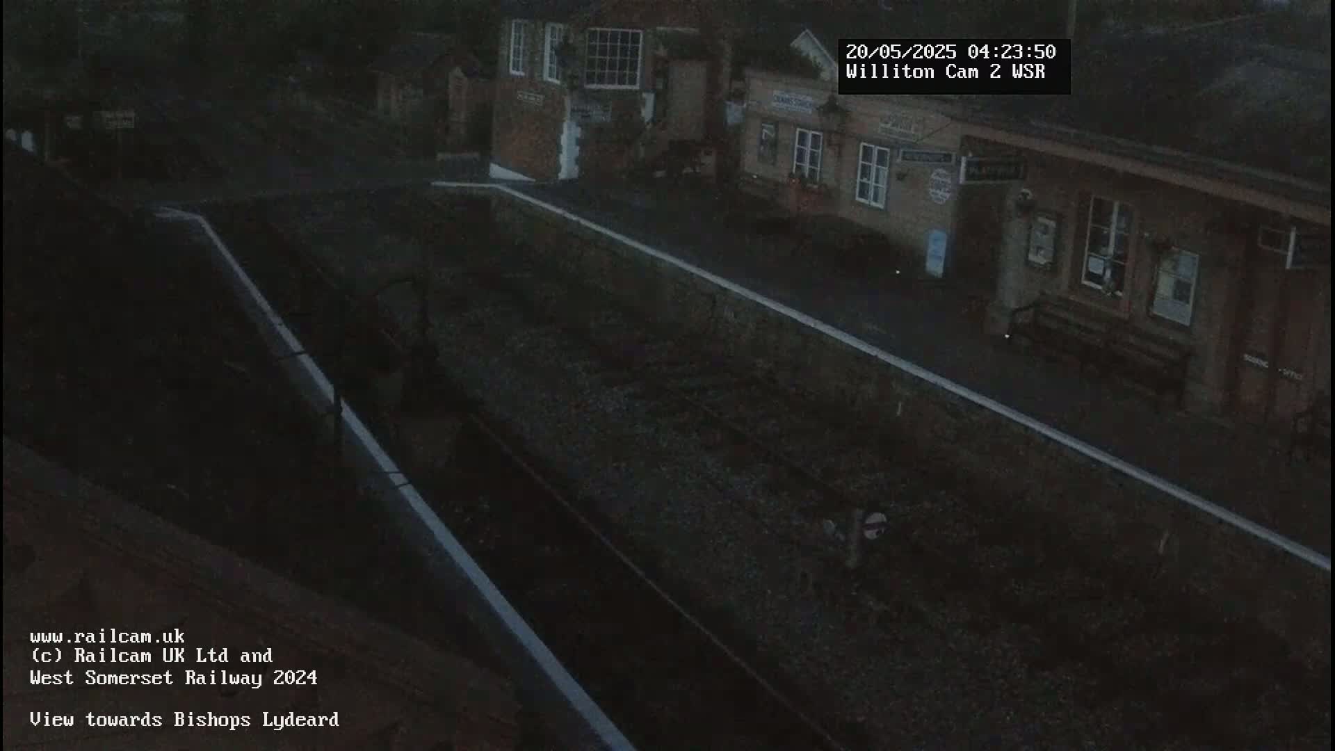 A dark, nighttime view of a train station platform and tracks.