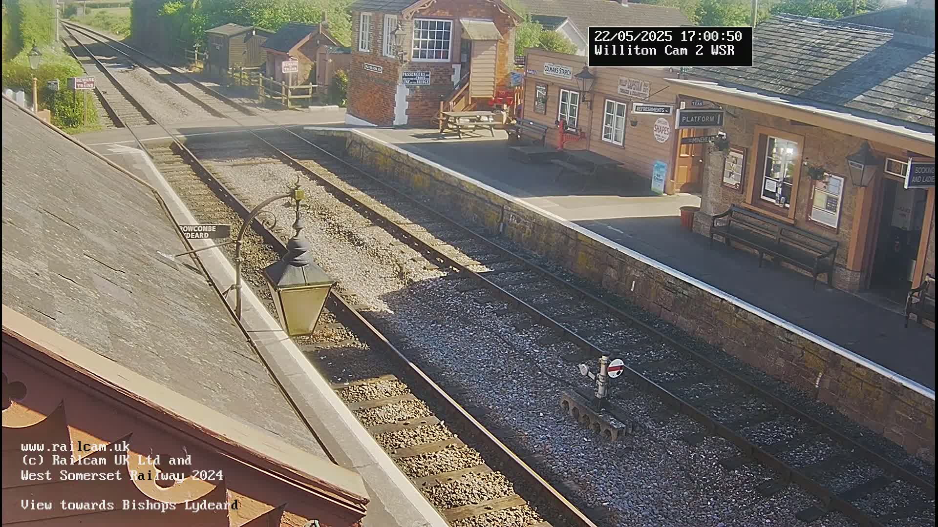 A sunny view of a train station platform with two parallel train tracks extending into the distance.