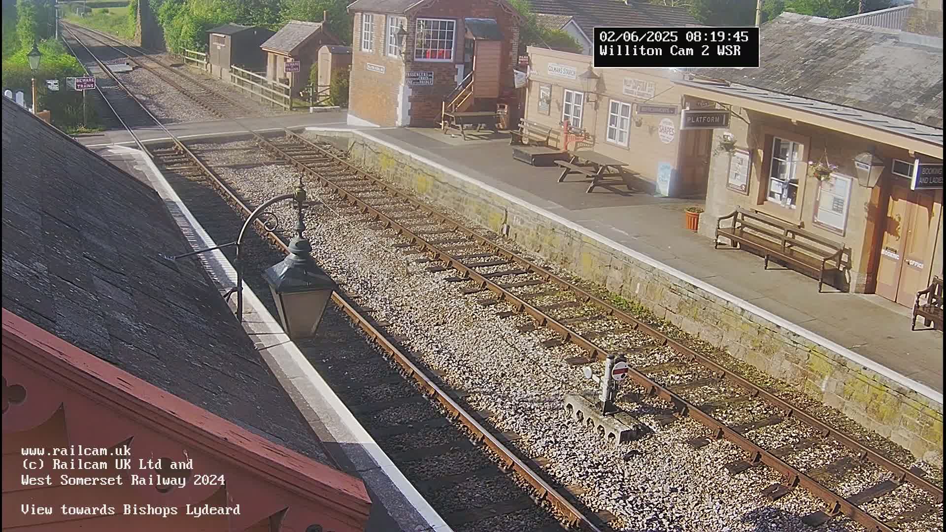 A sunny view of a train station platform with a railway track extending into the distance.