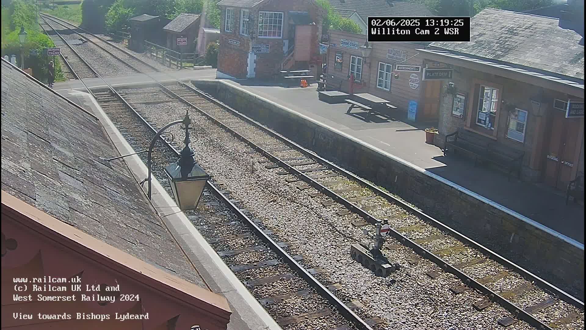 A high-angle view of a train station platform on a sunny day, showing train tracks extending into the distance and a small railway maintenance vehicle on the tracks.
