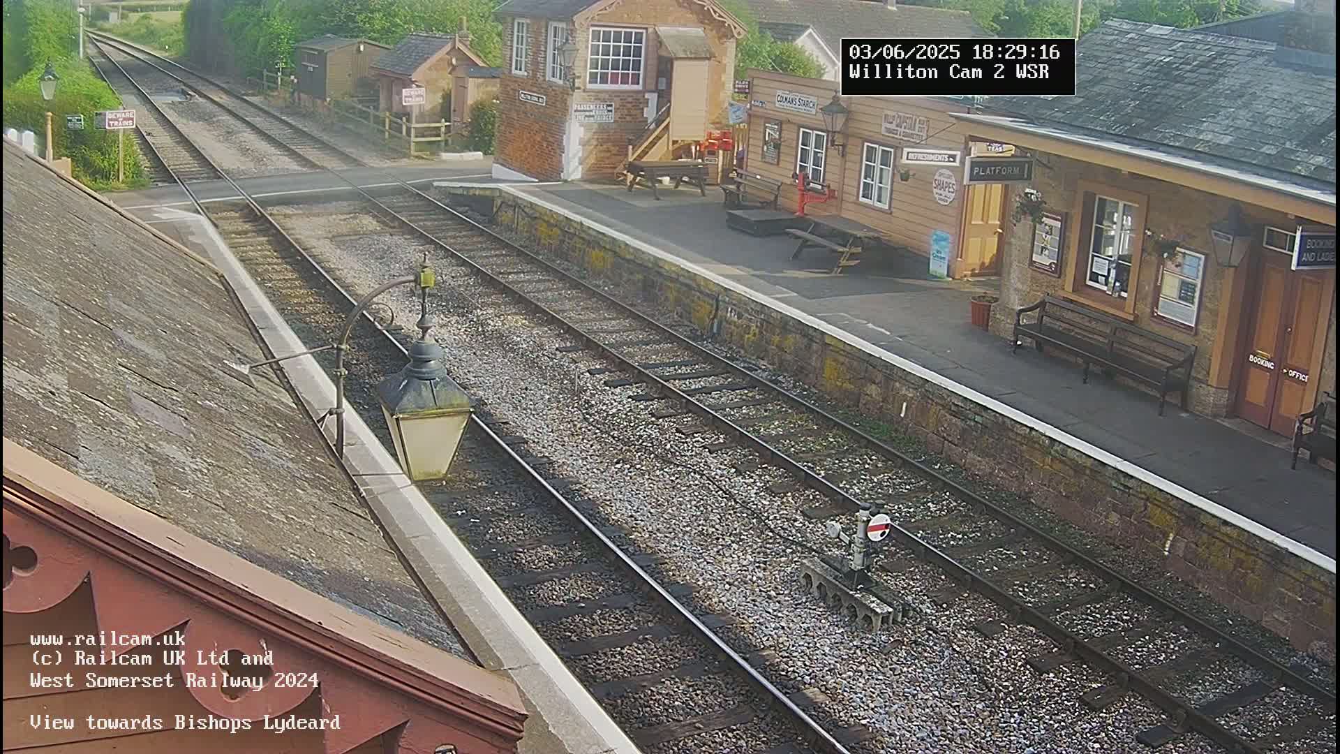 A view of a train station platform with railway tracks extending into the distance on a sunny day.