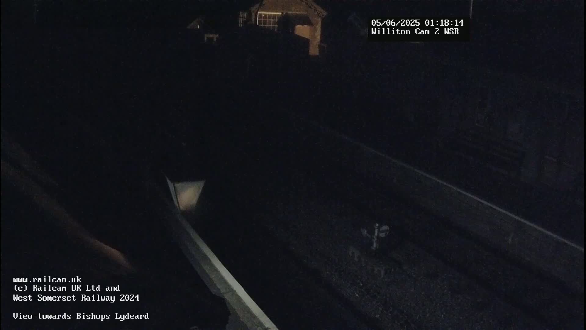 A nighttime view of a dark railway track, with a dimly lit building visible in the distance.