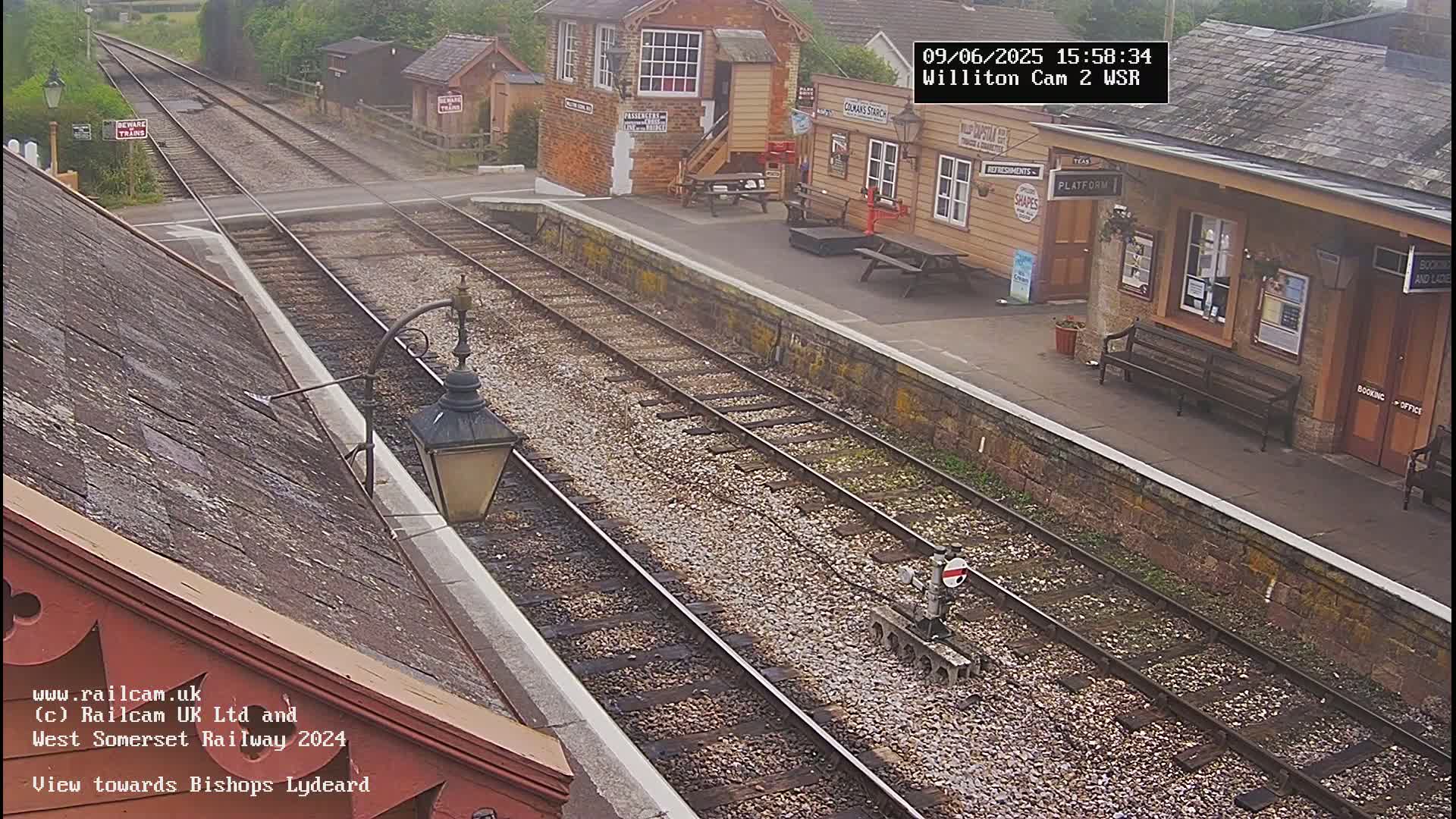 A train station with two tracks and a platform, viewed from an elevated perspective on an overcast day.