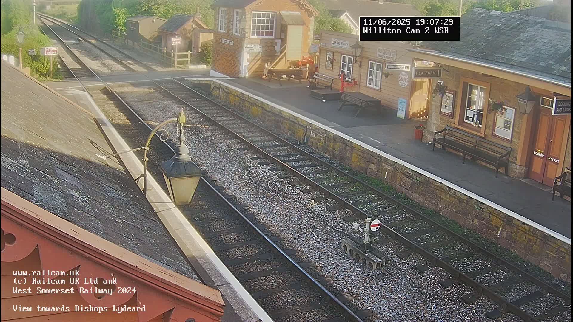 A sunny view of a train station platform with two sets of train tracks and a building.