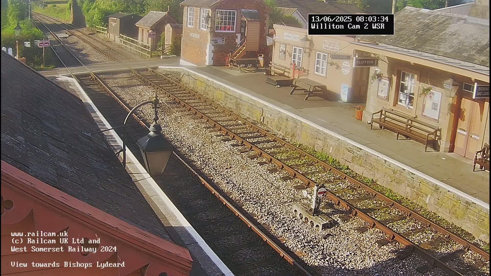 A sunny view of a train station platform with multiple train tracks extending into the distance.