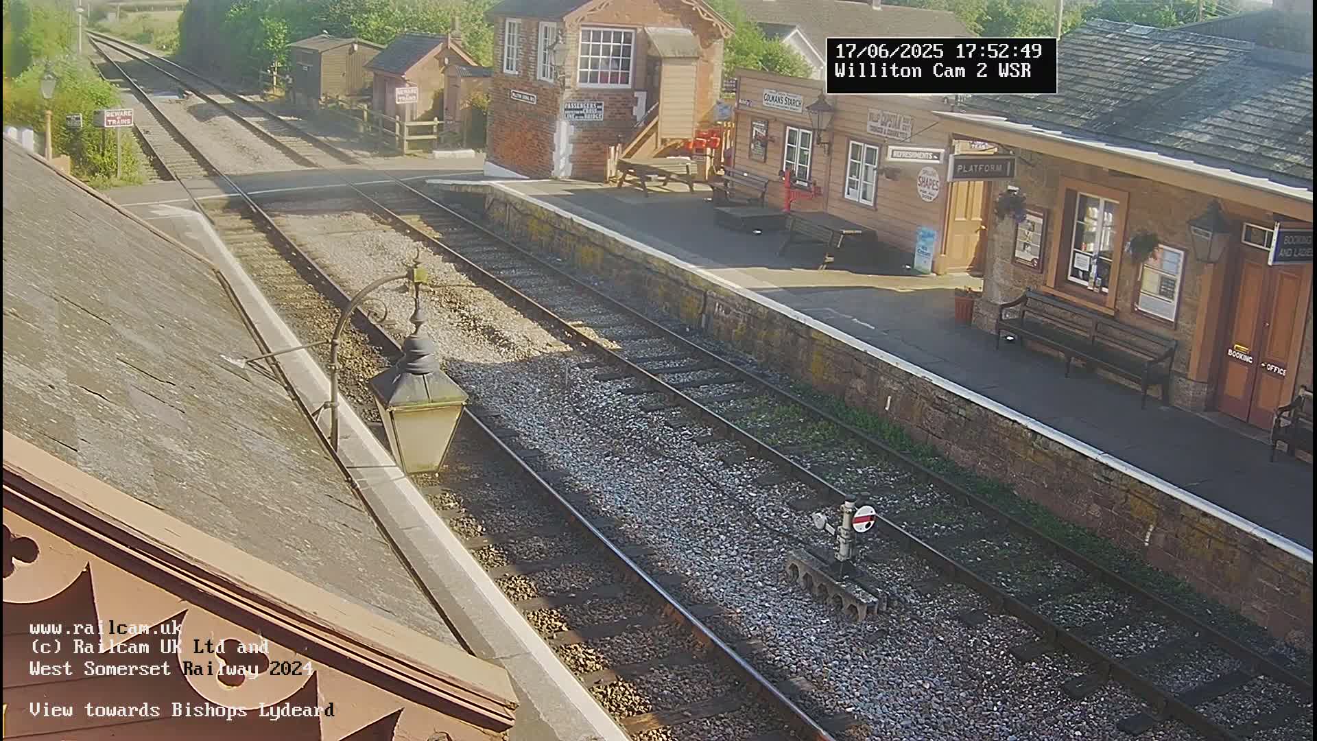 A sunny view of a train station platform with two train tracks extending into the distance.