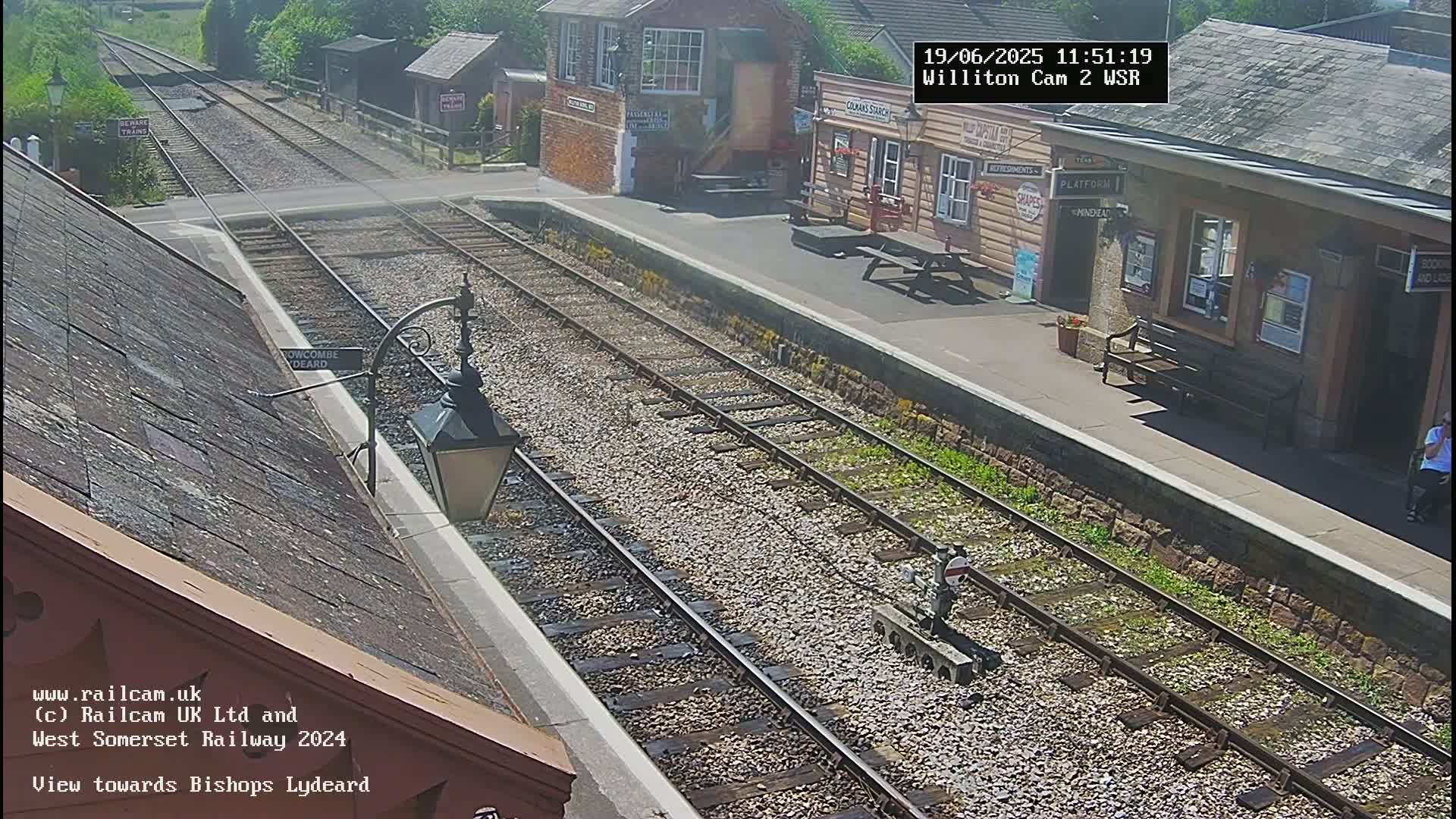 A sunny view of a train station platform with train tracks extending into the distance.