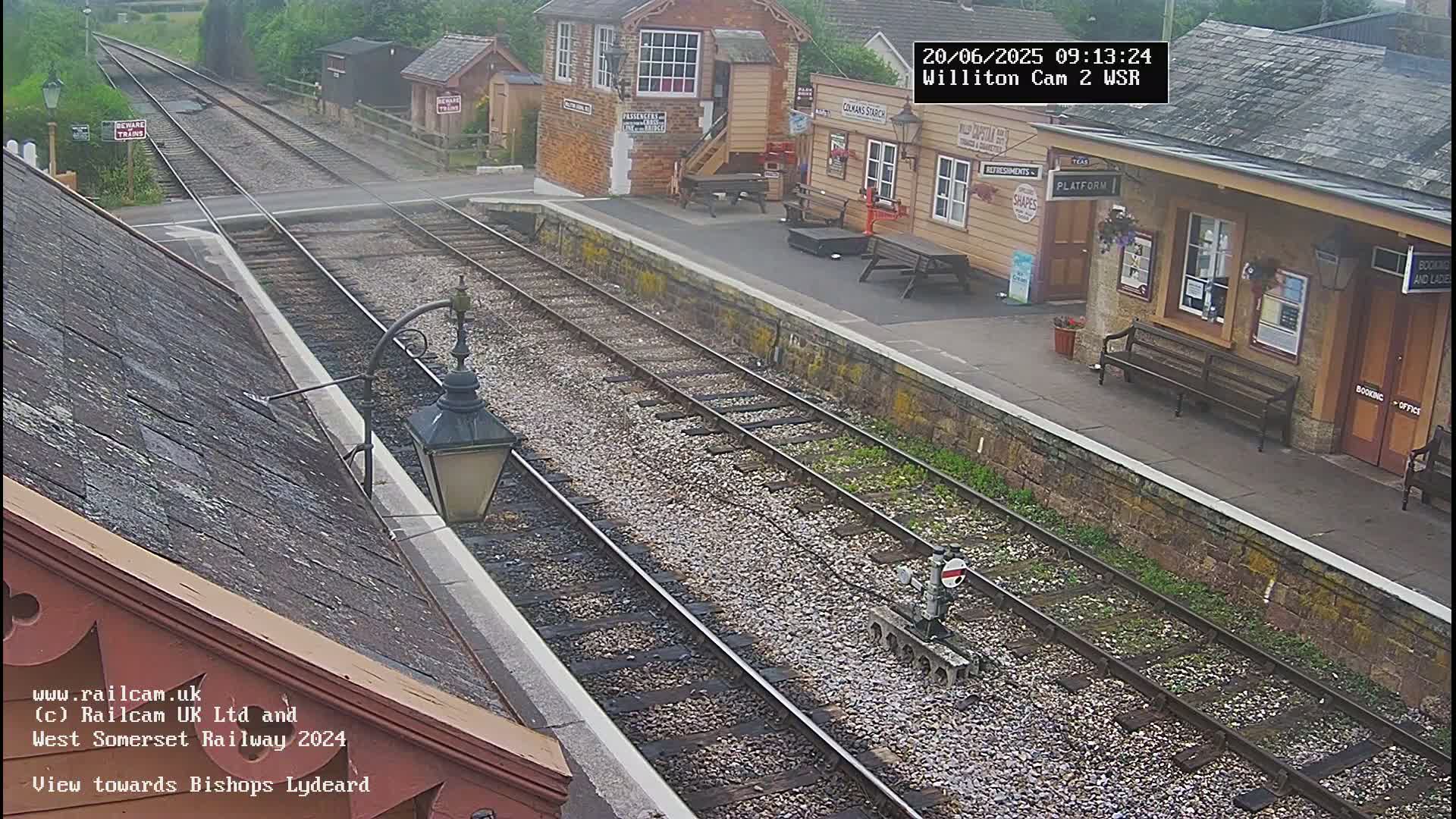 A train station platform with two sets of tracks is visible on an overcast day.