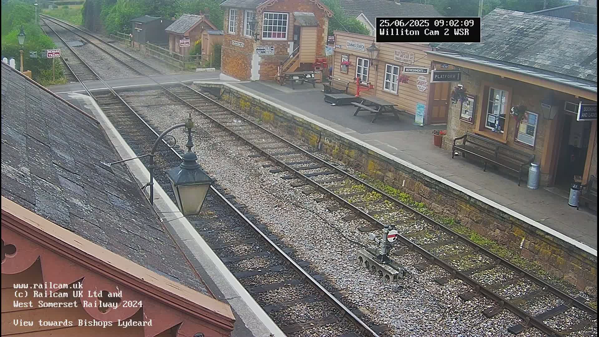 A train station platform with multiple train tracks, a small building, and a bench, viewed on an overcast day.