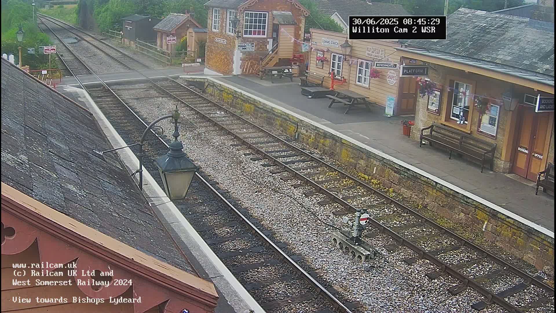 An overcast view of a train station platform with train tracks, a small building, and benches.