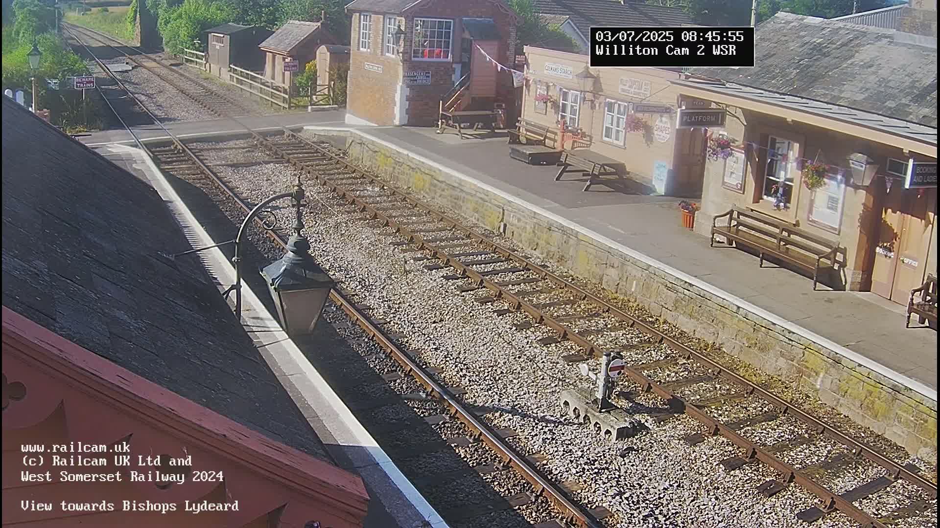 A sunny view of a train station platform with train tracks extending into the distance.