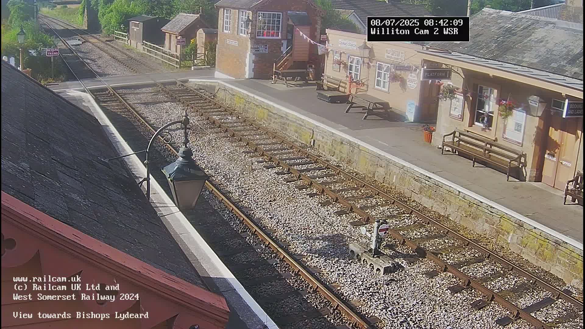 A sunny view of a train station platform with train tracks extending into the distance.