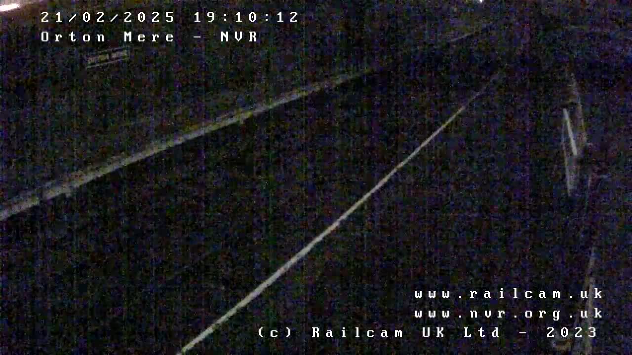 A nighttime, low-angle view shows a dark, seemingly empty railway track.