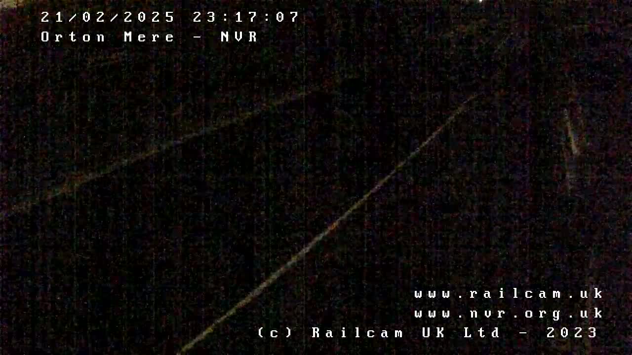 A dark, nighttime image shows a dimly lit, possibly paved, surface with faint diagonal lines.