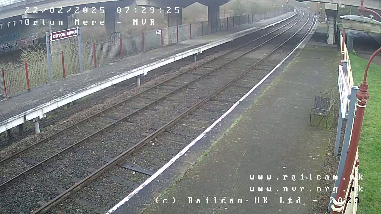A mostly empty train platform on an overcast day, with train tracks extending into the distance.