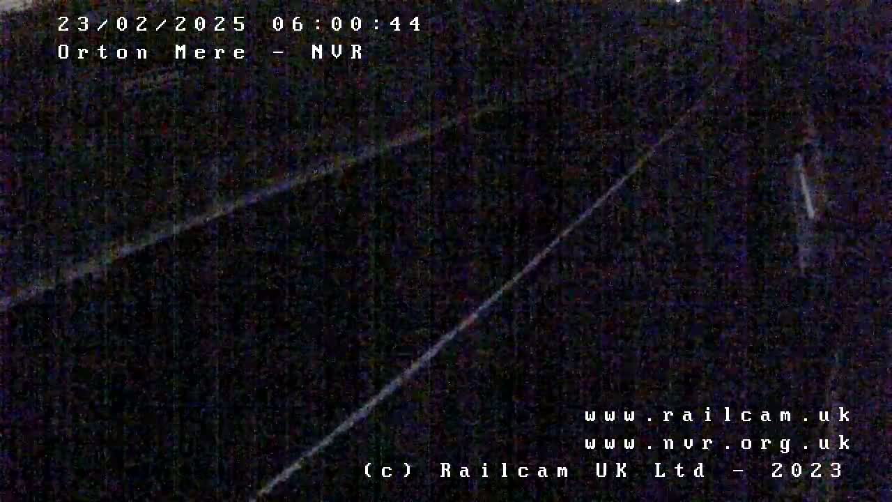 A nighttime, low-light view of a dark, possibly railway, scene with two bright diagonal lines.