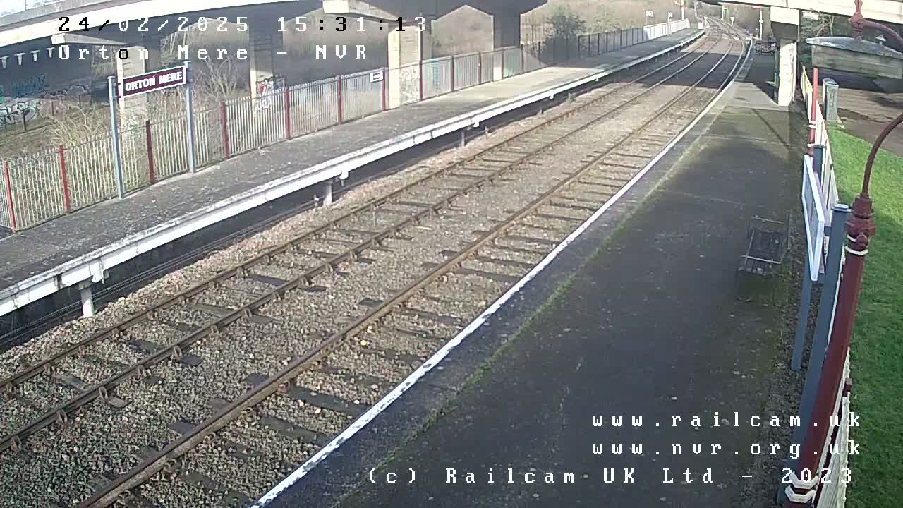 A train platform with railway tracks extending into the distance on a sunny day.