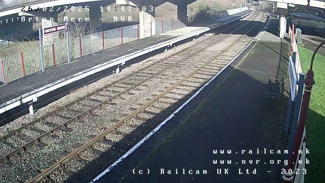 A sunny view of a mostly empty train platform with railway tracks extending into the distance.