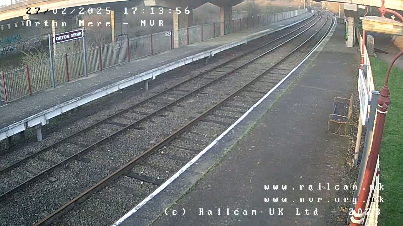 A train platform with two railway tracks stretches into the distance under an overcast sky.