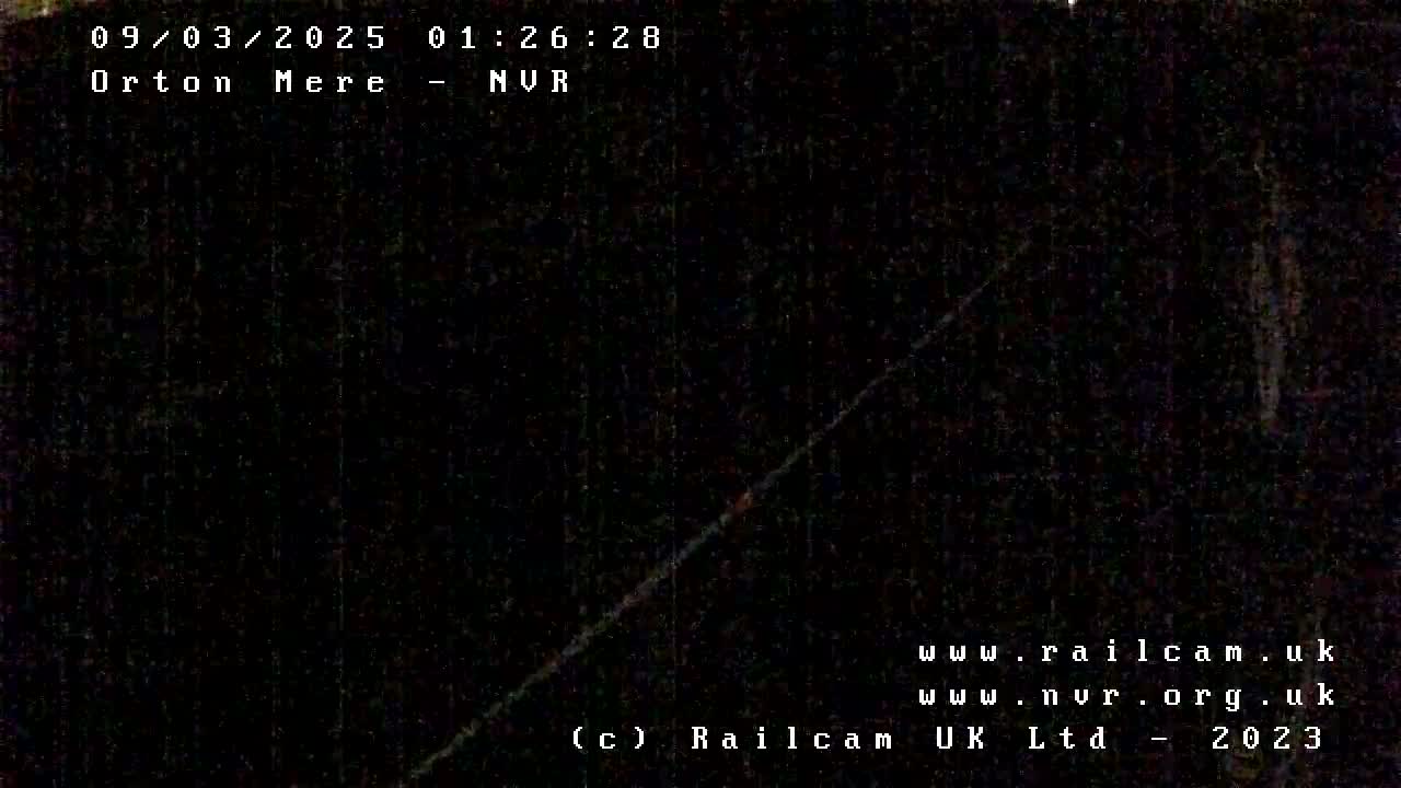A dark, nighttime image shows a dimly lit, possibly outdoor scene with a diagonal line, possibly a wire or track, against a very dark background.