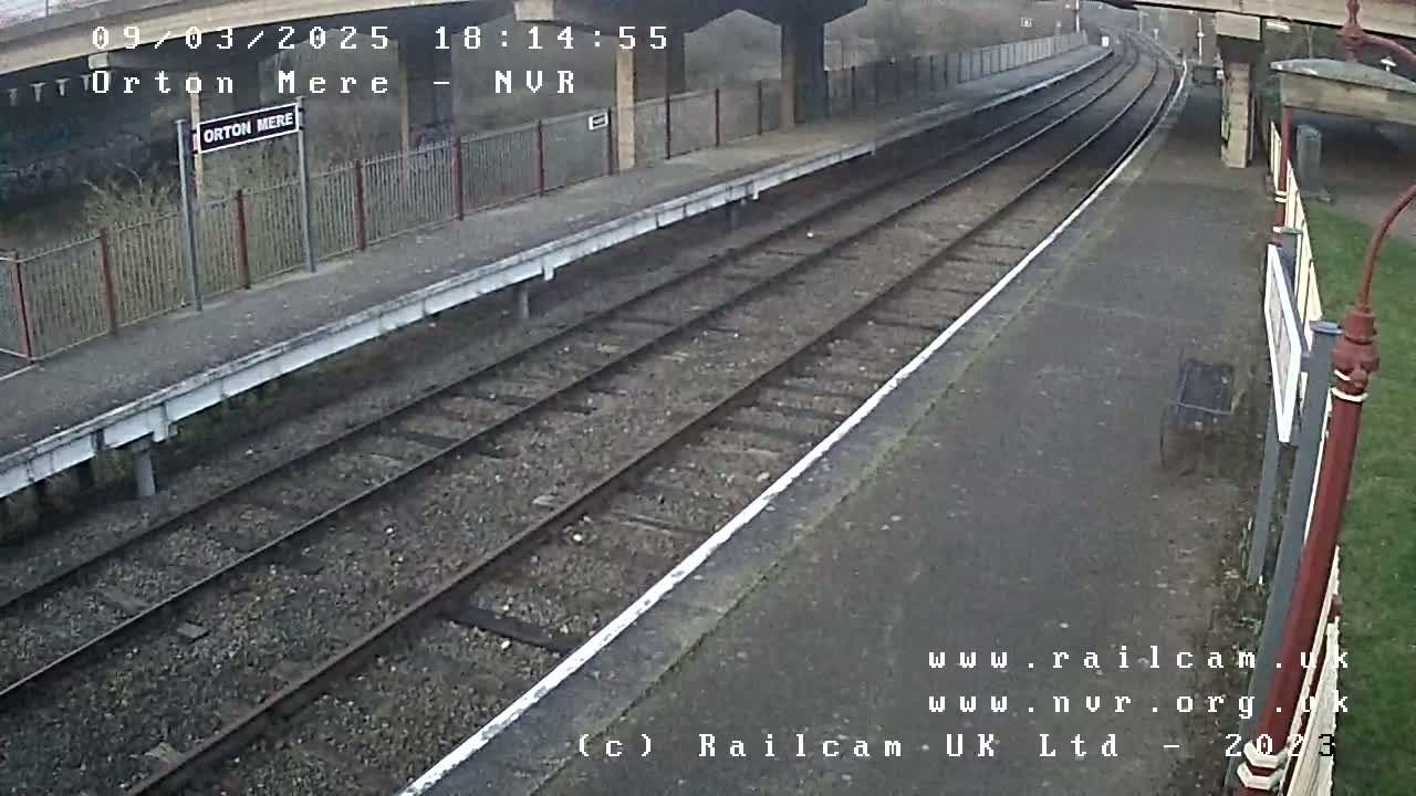A mostly empty train platform on an overcast day is seen next to two sets of train tracks.