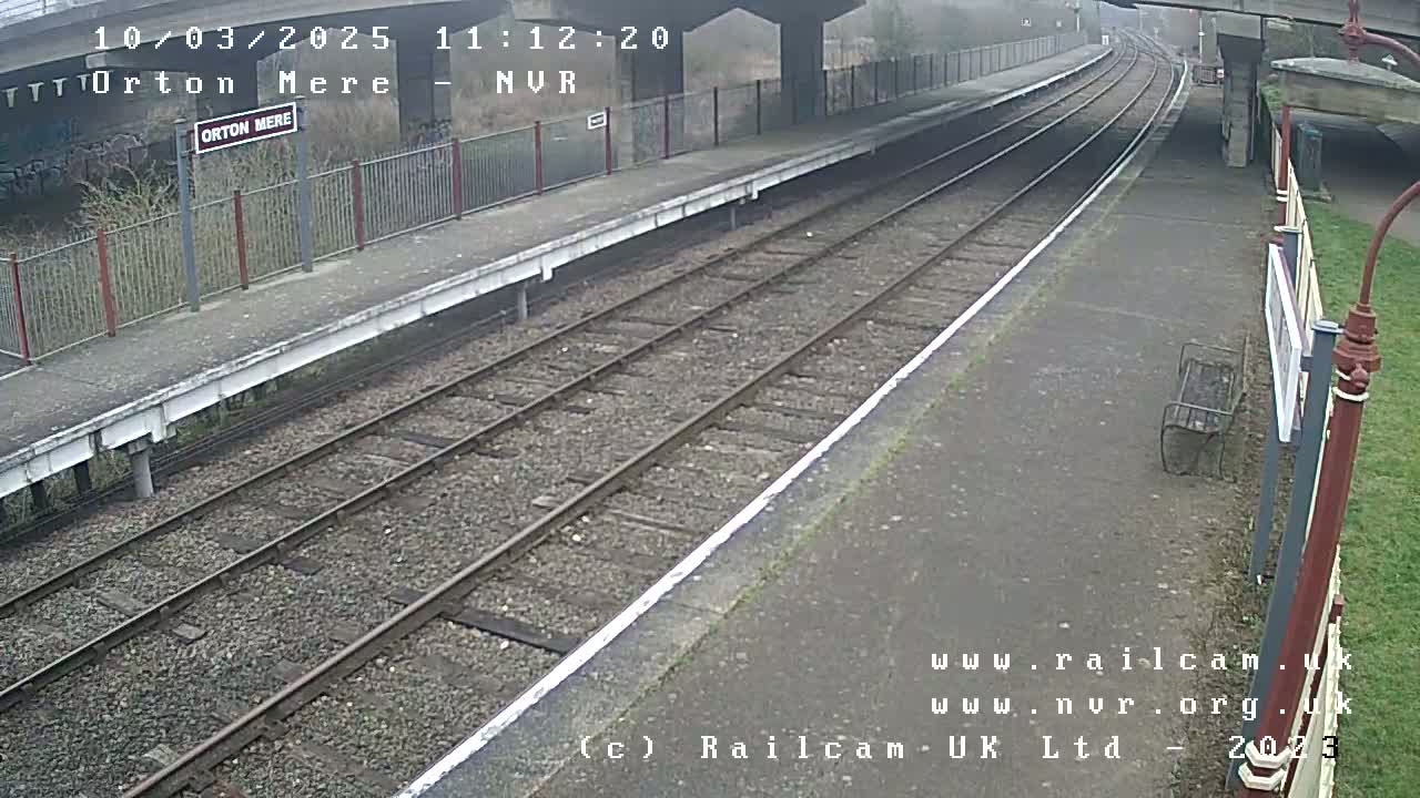 A mostly overcast view of a deserted train platform with two sets of train tracks.
