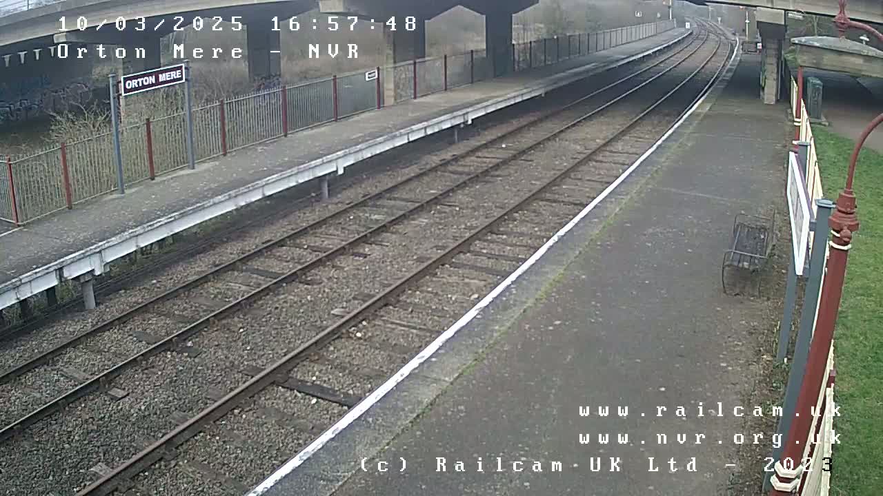 A mostly empty train platform with two train tracks under an overcast sky.