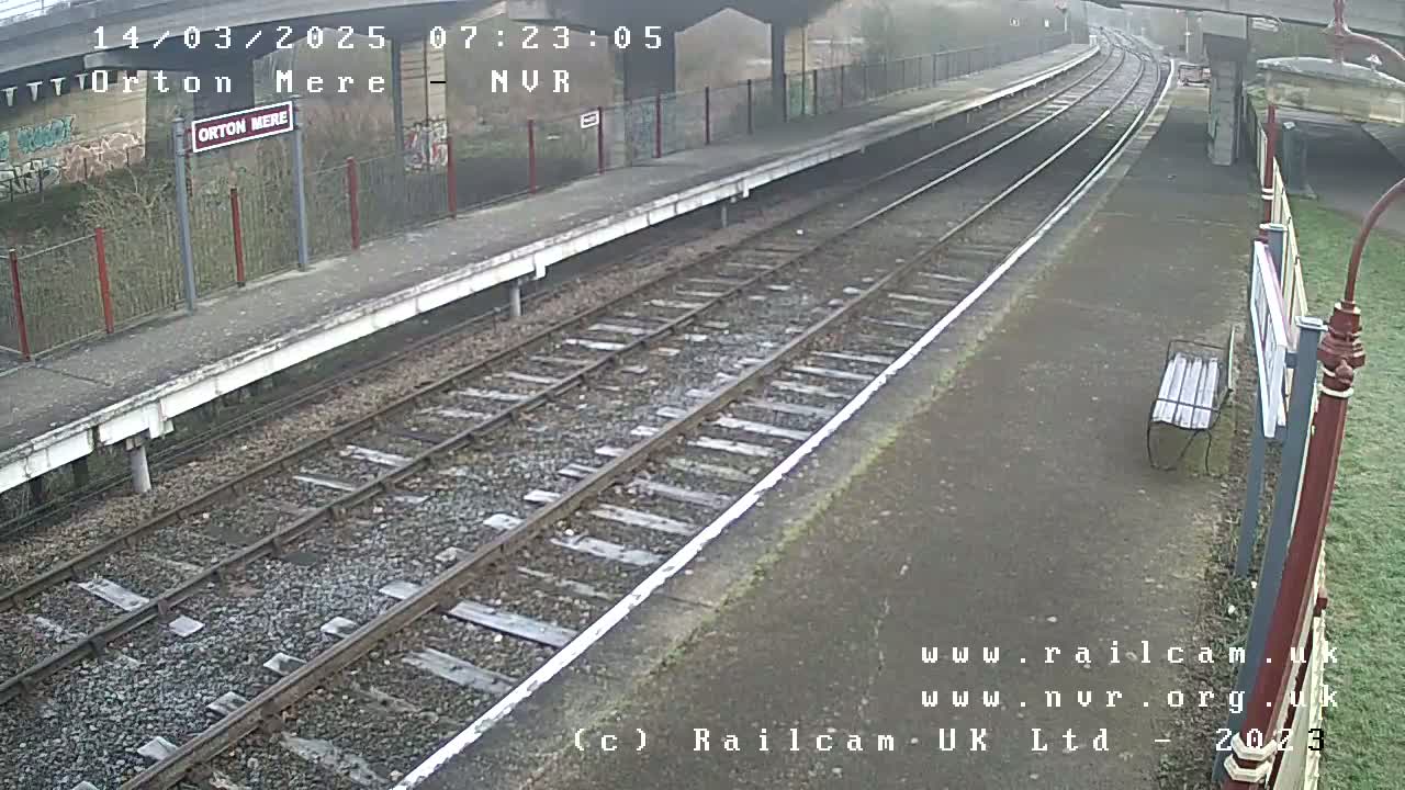 A mostly empty train platform on an overcast day with train tracks extending into the distance.