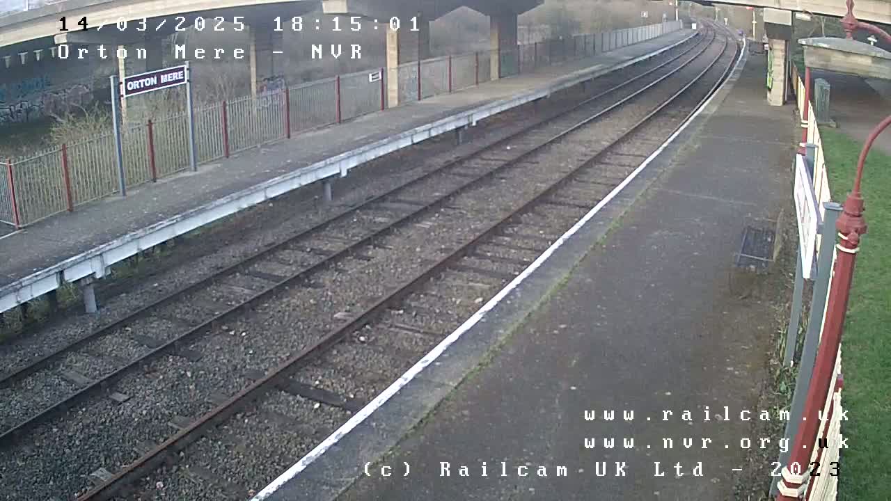 A mostly empty train platform with two sets of tracks under an overcast sky.