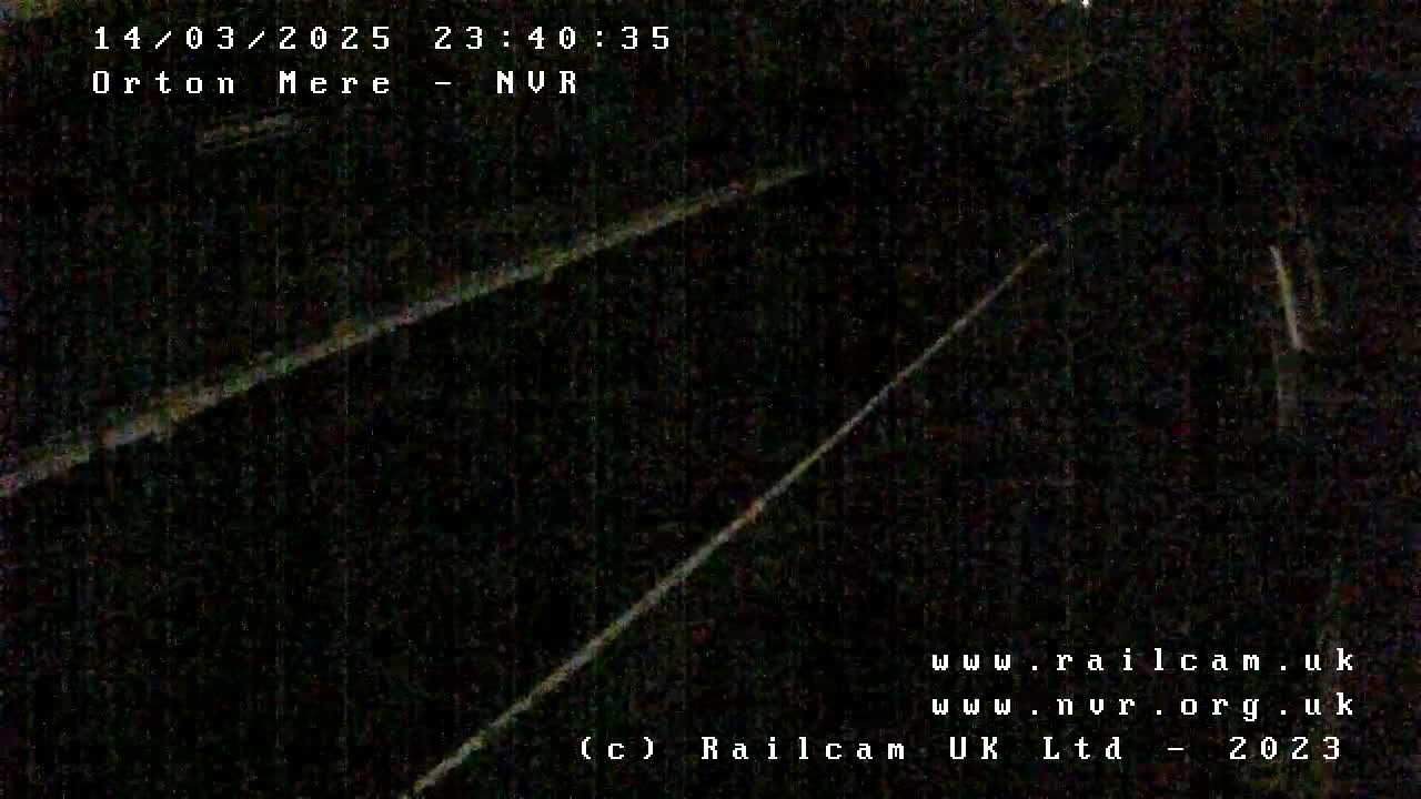 A nighttime, low-light image shows two parallel lines, possibly train tracks, extending into the darkness.