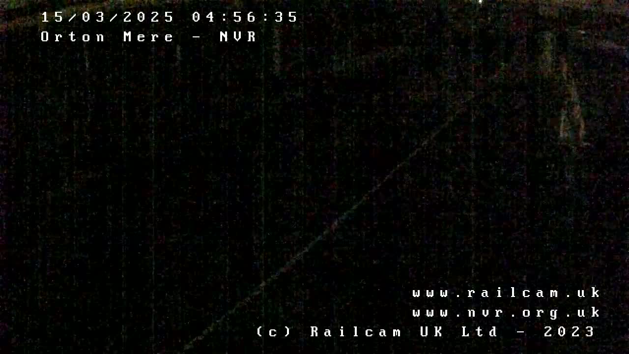 A nearly entirely dark nighttime image shows a dimly lit diagonal line, possibly a road or railway track, cutting across a dark, indistinct background.