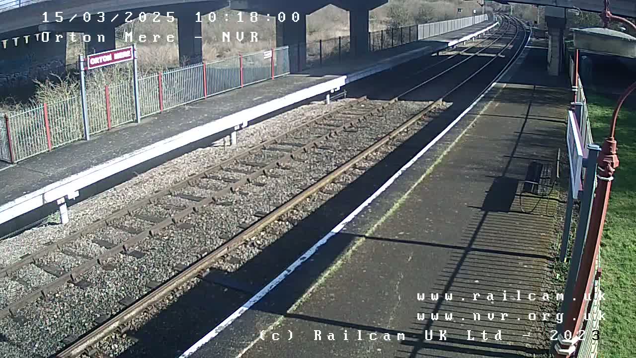 A sunny view of a train station platform with two sets of train tracks.