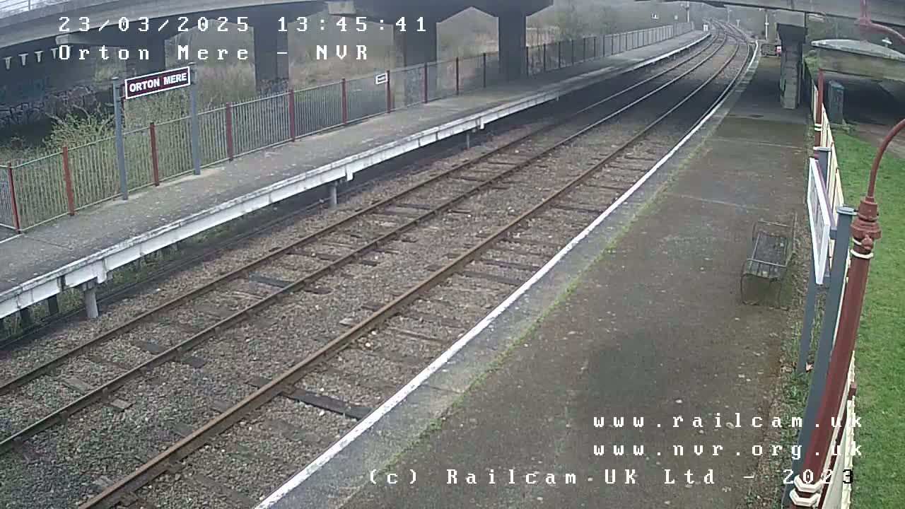 A train platform with two sets of railway tracks stretches into the distance under an overcast sky.